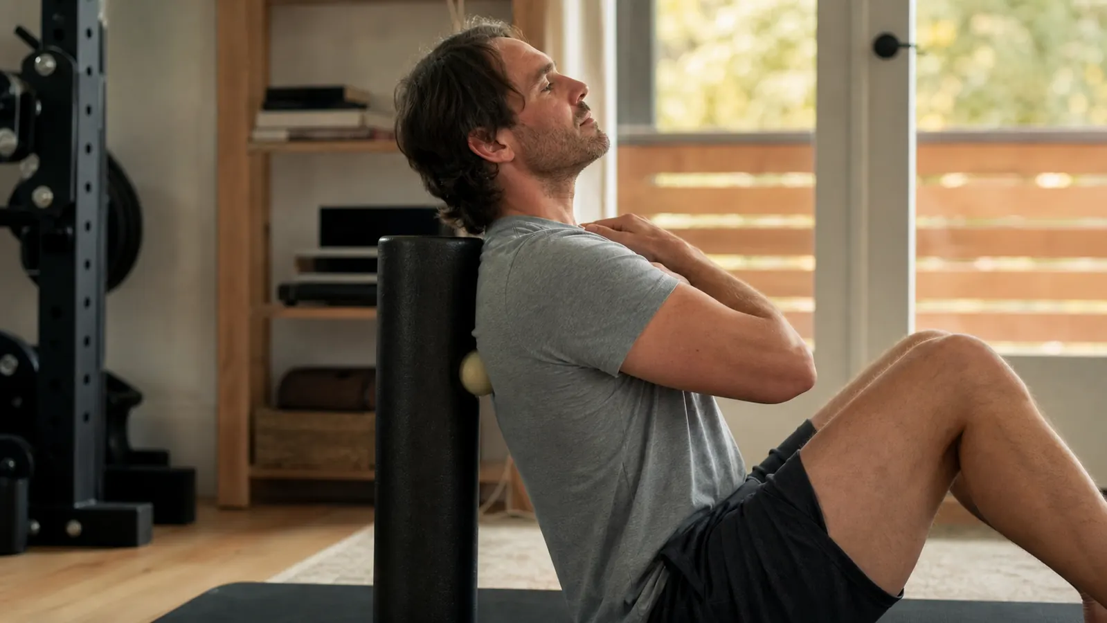 Man sitting on a gym bench pressing a lacrosse ball into his upper trap to release a knot